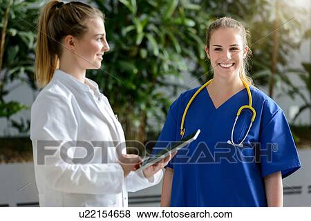 Two female junior doctors using digital tablet outside hospital, portrait View Large Photo Image Stock Photo - Two female junior doctors using digital tablet outside hospital, portrait. Fotosearch
