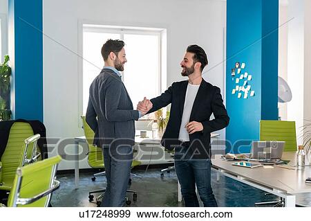 Stock Photo - Two male business creatives smiling and shaking hands in office. Fotosearch