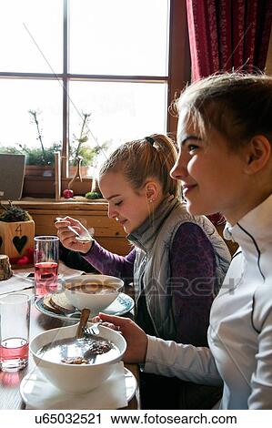 Stock Image - Two teenage girl skiers eating meal in cabin. Fotosearch