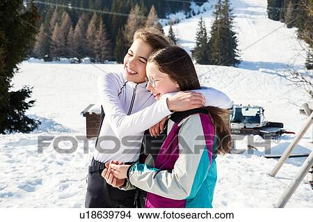 Picture - Two teenage girl skiers hugging in snow covered landscape, rear view, Tyrol, Styria, Austria. Fotosearch