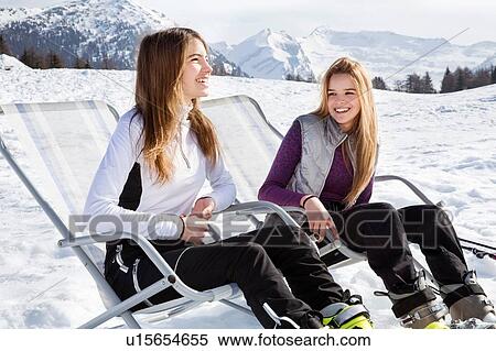 Stock Photography - Two teenage girl skiers sitting in deck chairs in snow covered landscape, Tyrol, Styria, Austria. Fotosearch