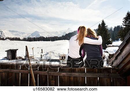 Two teenage girl skiers sitting on cabin roof terrace in snow covered landscape, rear view, Tyrol, Styria, Austria View Large Photo Image Stock Image - Two teenage girl skiers sitting on cabin roof terrace in snow covered landscape, rear view, Tyrol, Styria, Austria. Fotosearch