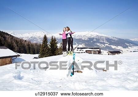 Stock Photo - Two teenage girl skiers standing on top of snow mound in snow covered landscape, Tyrol, Styria, Austria. Fotosearch