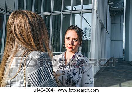 Stock Photo - Two young businesswomen talking outside office building, over shoulder view, Turin, Piemonte, Italy. Fotosearch