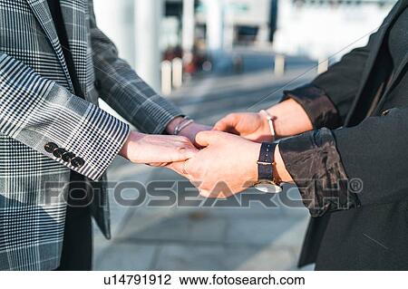 Stock Image - Two young women holding hands on city sidewalk, cropped mid section. Fotosearch