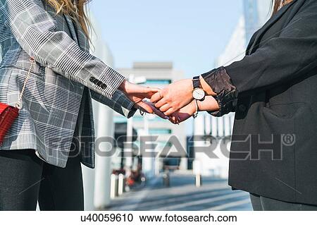Stock Image - Two young women holding hands outside office building, cropped, Turin, Piemonte, Italy. Fotosearch