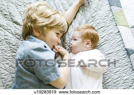 Stock Photo - View directly above boy with his baby brother lying on bed. Fotosearch