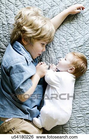 Stock Photograph - View directly above boy with his baby brother lying on bed. Fotosearch