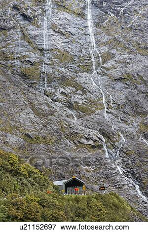 Stock Photo - Waterfall above building in Milford Sound, New Zealand. Fotosearch
