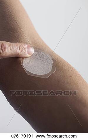 Stock Image - Woman applying a hormone replacement therapy (HRT) patch to her arm. This transdermal patch slowly administers the hormone oestrogen into the bloodstream. Oestrogen replacement therapy is typically given to relieve menopausal symptoms in women.. Fotosearch