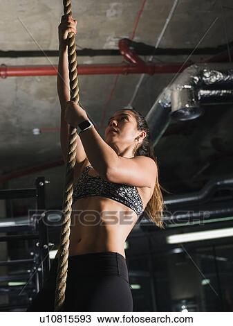 Stock Image - Woman climbing rope in gym. Fotosearch
