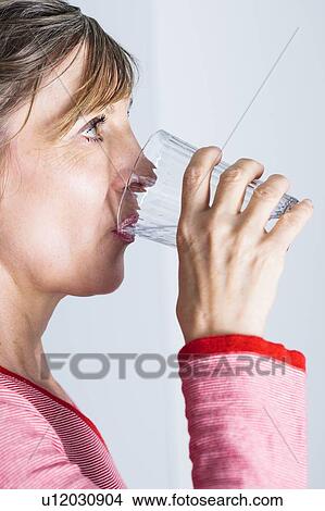 Picture - Woman drinking glass of water to hydrate.. Fotosearch