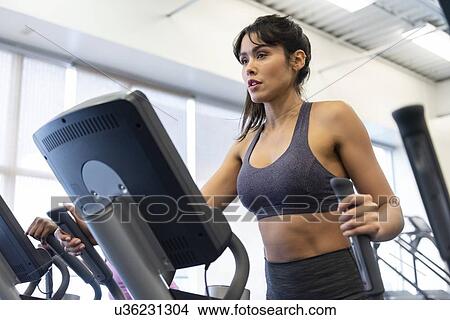 Picture - Woman exercising on elliptical machine. Fotosearch