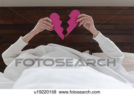 Woman holding aloft pink broken heart while lying in bed View Large Photo Image Stock Photo - Woman holding aloft pink broken heart while lying in bed. Fotosearch