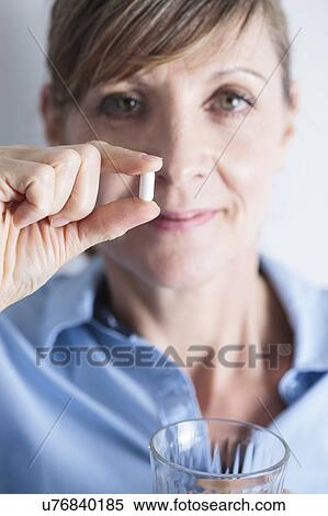 Stock Photography - Woman holding an ibuprofen tablet between her fingers.. Fotosearch