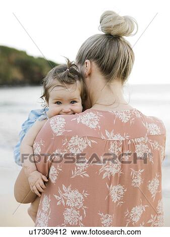 Stock Image - Woman holding baby daughter on beach. Fotosearch