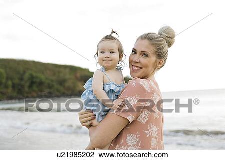 Stock Image - Woman holding baby daughter on beach. Fotosearch