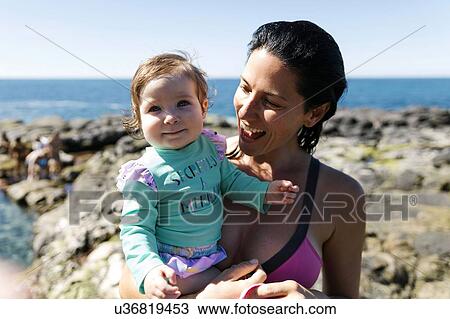 Woman holding baby daughter on rocks at beach View Large Photo Image Stock Image - Woman holding baby daughter on rocks at beach. Fotosearch
