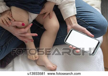 Stock Image - Woman holding daughter and smart phone. Fotosearch