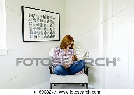 Stock Photo - Woman holding her newborn son on armchair. Fotosearch