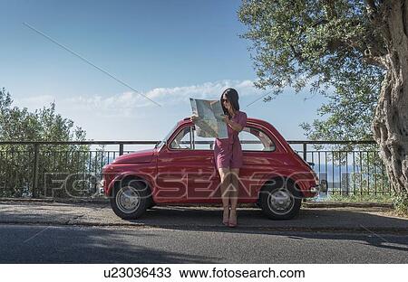 Stock Image - Woman holding map leaning on pink car. Fotosearch