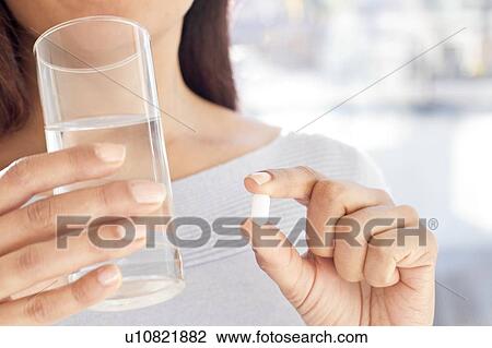 Stock Image - Woman holding painkiller tablet and glass of water.. Fotosearch