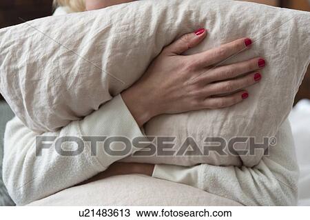 Stock Image - Woman holding pillow on bed. Fotosearch