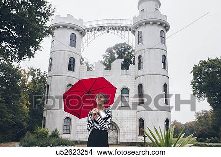 Picture - Woman holding red umbrella by Schloss Pfaueninsel in Potsdam, Germany. Fotosearch