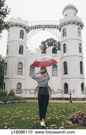 Stock Image - Woman holding red umbrella by Schloss Pfaueninsel in Potsdam, Germany. Fotosearch
