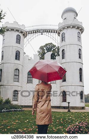 Stock Photo - Woman holding red umbrella by Schloss Pfaueninsel in Potsdam, Germany. Fotosearch