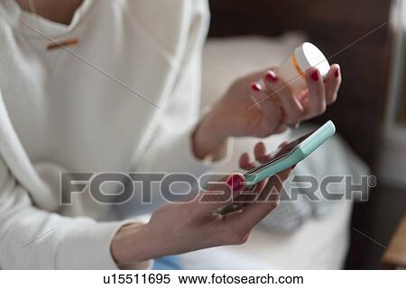 Stock Photography - Woman holding smart phone and pill bottle. Fotosearch
