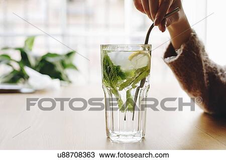 Stock Image - Woman holding straw in cocktail with mint leaves and lemon. Fotosearch