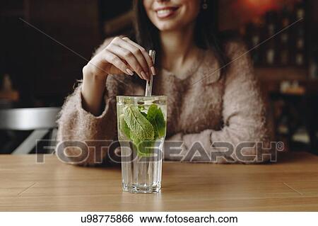 Stock Photograph - Woman holding straw in cocktail with mint leaves. Fotosearch
