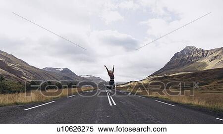 Stock Photography - Woman jumping on highway in Iceland. Fotosearch