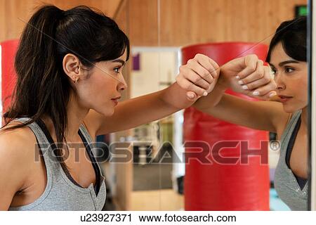 Stock Image - Woman leaning on mirror in gym. Fotosearch