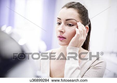 Picture - Woman looking in mirror in clinic.. Fotosearch