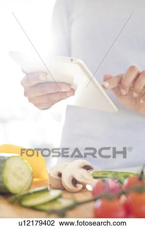 Stock Image - Woman preparing food using digital tablet.. Fotosearch