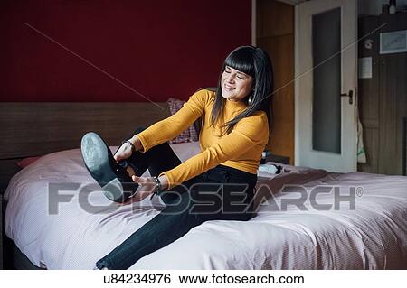 Stock Photograph - Woman putting on shoes in bed. Fotosearch
