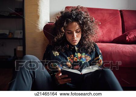 Woman reading book while leaning against sofa View Large Photo Image Picture - Woman reading book while leaning against sofa. Fotosearch