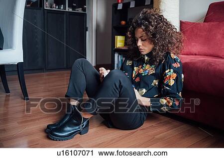 Woman reading book while leaning against sofa View Large Photo Image Stock Image - Woman reading book while leaning against sofa. Fotosearch
