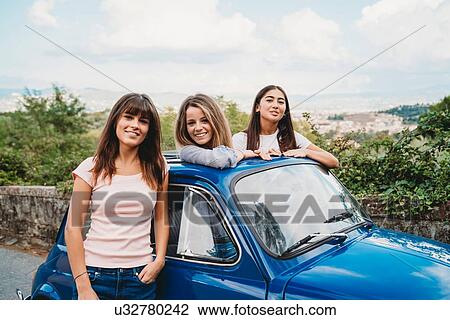 Stock Image - Woman standing beside friends posing in car sunroof, Florence, Toscana, Italy. Fotosearch