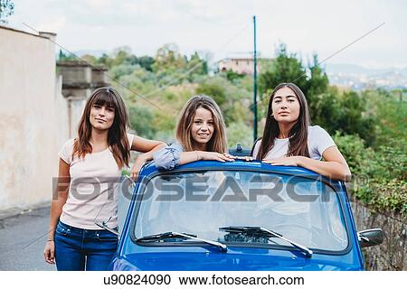 Stock Image - Woman standing beside friends posing in car sunroof, Florence, Toscana, Italy. Fotosearch