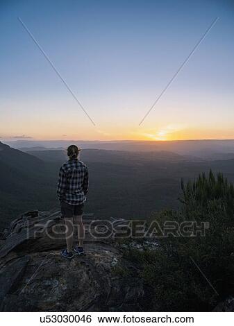 Stock Photograph - Woman standing on peak of Blue Mountains at sunrise in New South Wales, Australia. Fotosearch