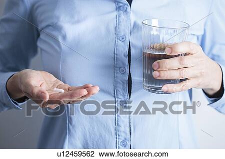 Stock Image - Woman taking medication with a glass of water.. Fotosearch