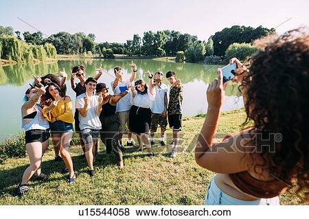 Stock Photo - Woman taking photograph of friends by lake. Fotosearch