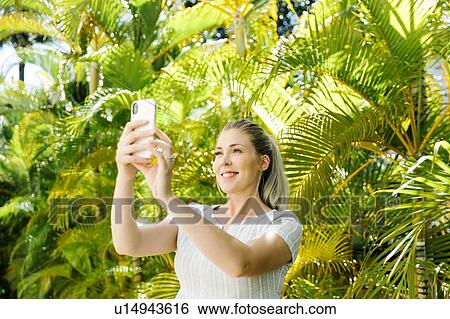 Stock Photograph - Woman taking selfie by palm trees. Fotosearch