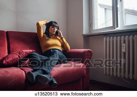 Stock Image - Woman talking on smartphone on sofa. Fotosearch
