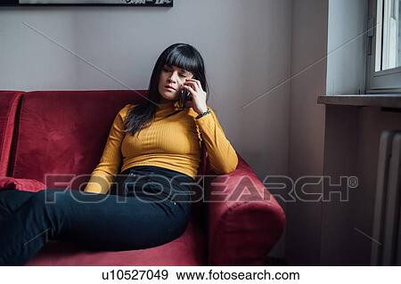 Stock Photo - Woman talking on smartphone on sofa. Fotosearch