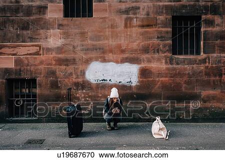 Stock Image - Woman texting on kerb with cellphone and luggage, Edinburgh, Scotland. Fotosearch