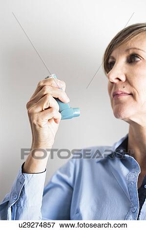 Stock Photo - Woman using an inhaler to treat an asthma attack. The inhaler contains bronchodilator drugs, which widen constricted airways in the lungs.. Fotosearch